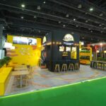 McCain booth at a trade show with yellow seating, a black central bar, and green-lit floor edge.