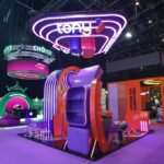 Colorful trade show booth with a neon purple 'tony' sign and futuristic purple&ndash;orange display elements illuminated by LEDs.