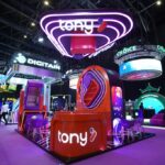 Colorful tech expo booth with neon purple Tony sign, circular light structures, and a red Tony kiosk at the center.